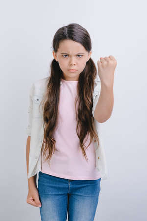 Little angry girl standing in the studio over white background and showing fist with her hand .- Imageの写真素材