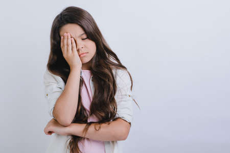 Portrait of a sleepy girl with long hair covering one eye with her hand.- Imageの写真素材