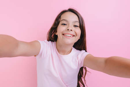 Closeup portrait of a cheerful girl over pink studio background with straightening handsの写真素材