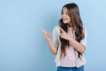 Closeup portrait of a cheerful happy little girl over blue studio background pointing her index finger up. - Imageの写真素材