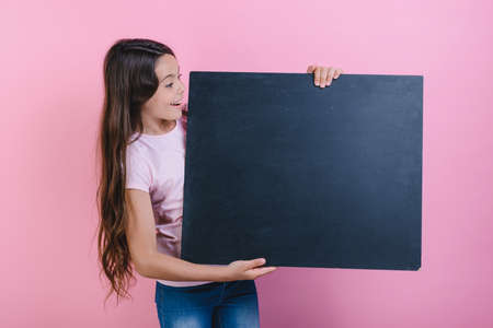 Schoolgirl stands holding a blackboard in her hands and looking in it . - Imageの写真素材