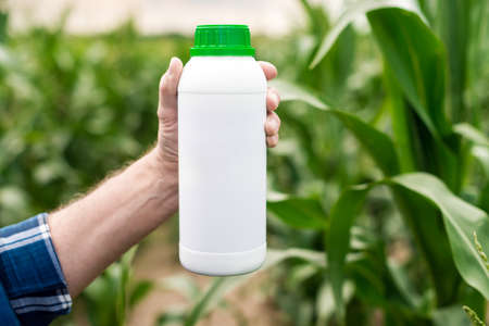 Bottle in male hands against the background of the field. Fertilizer bottle mockupの写真素材