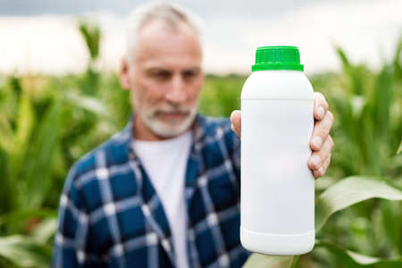 Middle aged farmer in a field showing a bottle with chemical  fertilizers. Focus on the bottleの写真素材
