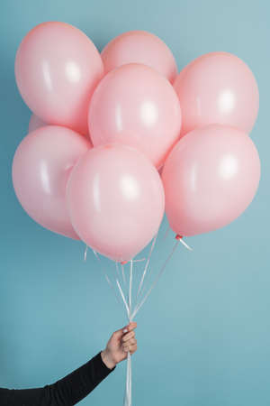 Pink air flying balloons in man hands isolated on blue background. Man in shirt holding many pink air balloons, free space. Summer, holidays, celebration, happy birthday and lifestyle conceptの写真素材