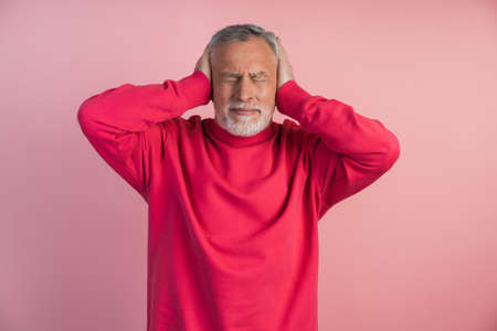 Man does not want to hear anything. Older man shows a gesture that he does not want to hear anything, he closes his ears with his hands, annoyed on a pink background.の写真素材