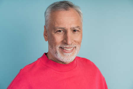 Close-up view, senior man smiling on blue background. Attractive man in a bright pullover.の写真素材