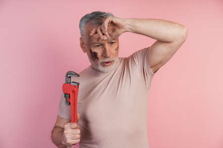 Tired man with a wrench in his hands grabbed his head. Man isolated on a pink background, tired of workの写真素材