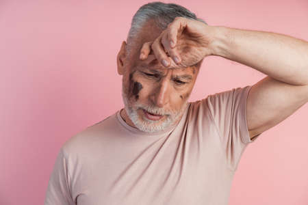 Close-up view of a tired man on a pink background. Senior man with a smeared face on a pink background.の写真素材