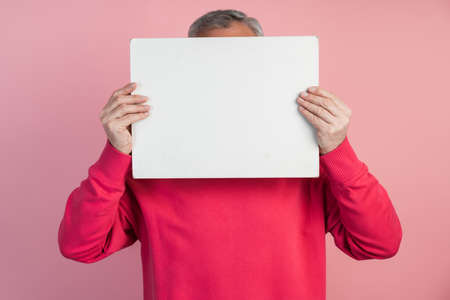 Man covers his face with a white sheet of paper. On a pink background copy space, place for text, advertising.の写真素材
