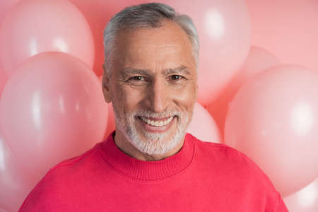 Sincere, attractive man smiling on a background of pink balloons. Holiday concept.の写真素材