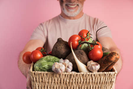 Close view, basket with vegetables, man holding fresh vegetables. Isolated on pink background,...