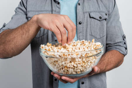Closeup  a plate of popcorn in male hands. Man takes bunch  of popcorn by his armの写真素材