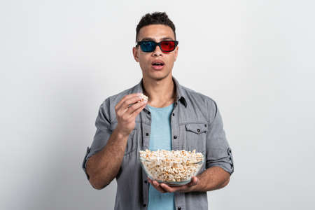 Man in the 3D glasses stands with a plate of popcorn in his hands  and looking opened his mouth amasedの写真素材