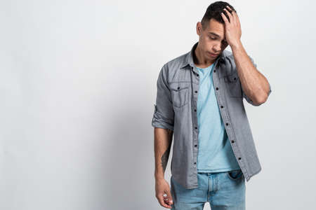 Portrait of a lamentablesad, mulatto man standing with his head down and touching his head with his handの写真素材