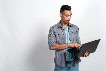 Serious mulatto man holding a laptop in his hands standing against white background.- Imageの写真素材