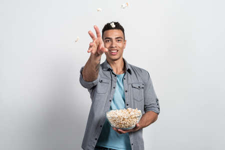 Mulatto man holding a plate of popcorn in his hands and throwing popcorn at the cameraの写真素材