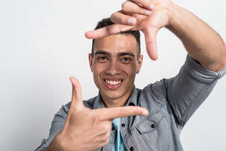 Closeup smiling face of mulatto man in the square from gesture with male  fingers.- Imageの写真素材