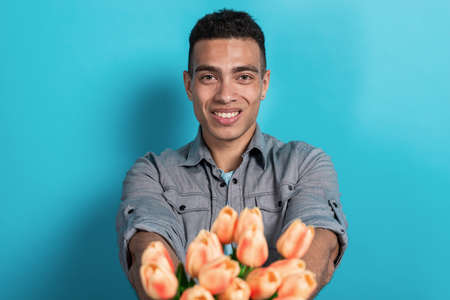 Happy mulatto man holding his hands straight himself with a tulips bouquet looking at the camera .- Imageの写真素材