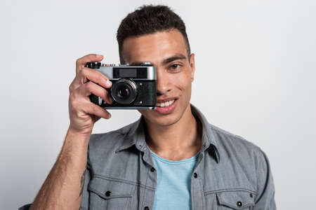 Smiling mulatto man holding a retro photocamera against his face and looking at the camera- Imageの写真素材
