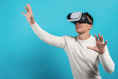 Close up of young  guy wearing  virtual reality headset on blue background in studio and...