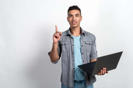 Mulatto man holding a laptop in his hands standing . Man has an idea pointing by index finger up-...