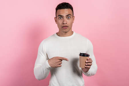Amazed guy holding a paper glass of coffee and pointing to it. Facial emotion- Imageの写真素材