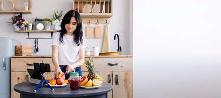 Beautiful brunette prepares fruit smoothie at home in the kitchen and removes the cooking process for her channelの写真素材