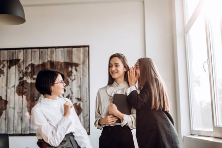 Concept of working, controversial issues. Three confident girls chatting in the office, one whispers in the other's earの写真素材