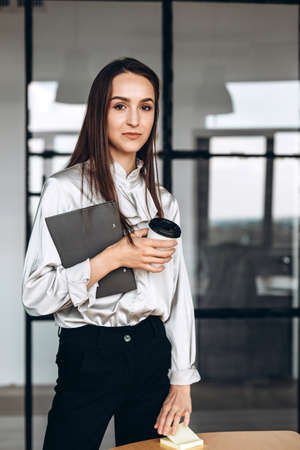 Pretty brunette with papers in her and cups of coffee, working in the officialの写真素材