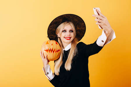 Cheerful woman take a selfie picture portrait against a yellow background  holding pumpkinの写真素材