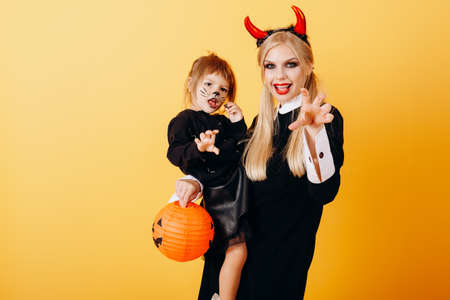 Happy emotion of devil woman standing against a yellow background and holding a little girlの写真素材