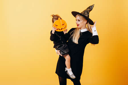 Woman in masquerade dress and hat posing against yellow background holding little girl - Imageの写真素材