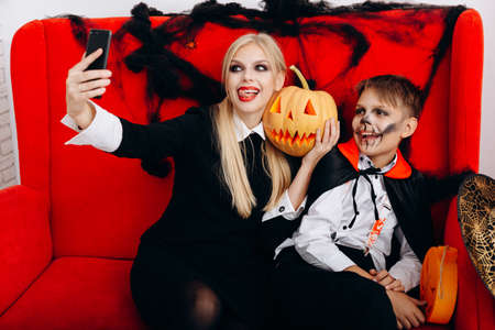 Mother and son have a funny time on red sofa and make a selfie closeup. Emotion and Halloween conceptの写真素材