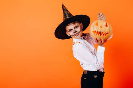 Portrait of boy in Devil masquerade makeup and hat  showing a pumpkin. Halloween conceptの写真素材
