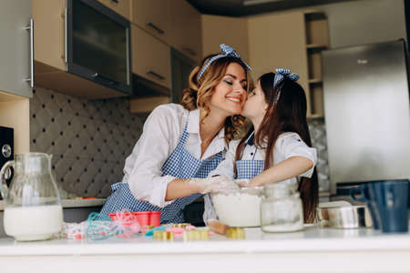 Daughter kissing her mother during cooking together in the kitchen. - Imageの写真素材