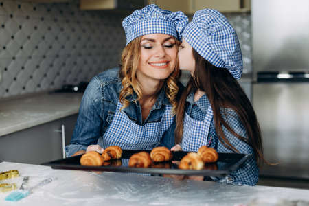 Daughter and mother baked croissants. Girl kissing her happy mother. Family concept- Imageの写真素材