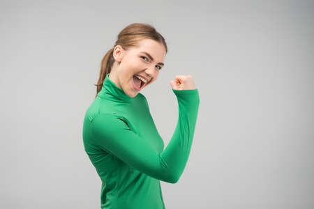 Happily gladden young woman looking at the camera with cleanch fist up and smiling with opened mouth .- Imageの写真素材