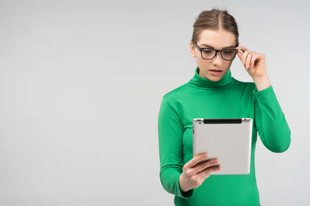 Girl surprised in profile looks on a tablet standing. - Front view