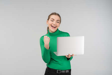 Enthusiastic young woman looking at laptop with victorious expression . Holds device and fist up. - Concept imageの写真素材