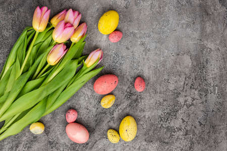 bouquet of tulips and colorful eggs lie in the corner on grey plaster background, empty copyspaceの写真素材
