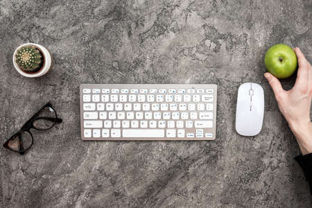 Top view keyboard, glasses, mouse and a fresh green apple in male handの写真素材