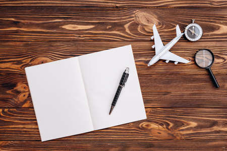 On a wooden surface a blank sheet of paper and a pen, an airplane and a compass, travel concept. High quality photoの写真素材