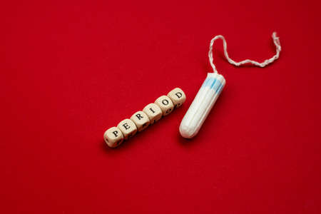 Tampon lying isolated on red background with text period. Concept women sanitary protectの写真素材