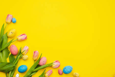 Tulips and colorful eggs lie in the corner on yellow Easter background, empty copyspaceの写真素材