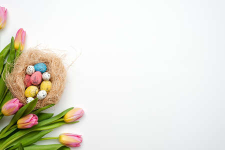 Easter background, multi-colored eggs and bouquet of tulips lie on a white table. - Copy spaceの写真素材