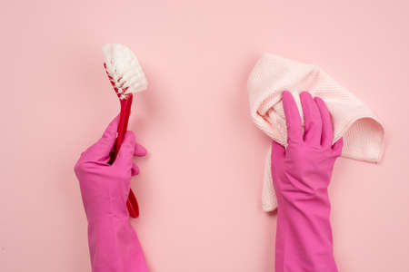 Closeup hands wearing in latex gloves holding a rag and household brush. Top view on pink backgroundの写真素材