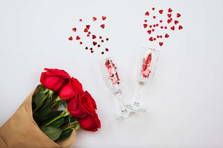 Beautiful composition. Bouquet of red roses and two wineglasses with hearts on a white backgroundの写真素材