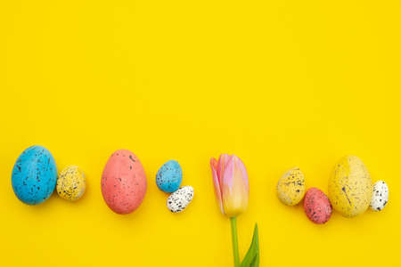 One tulip and colorful eggs lie on yellow Easter background, copyspaceの写真素材