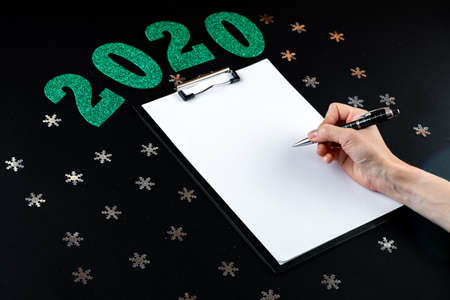 Female writing christmas greeting card on black background. Top view with copy spaceの写真素材