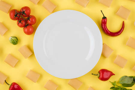 Empty plate on yellow background with pasta, tomatoes, pepper.の写真素材